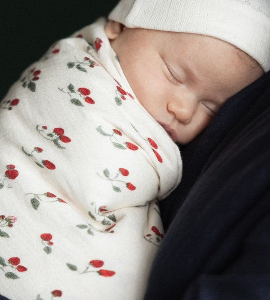 Newborn baby swaddled in a floral blanket with a white hat on.