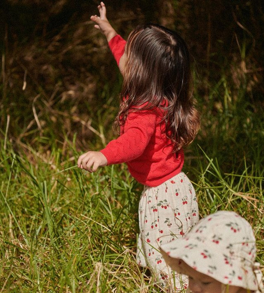 Child in a red sweater and floral dress standing in a grassy field