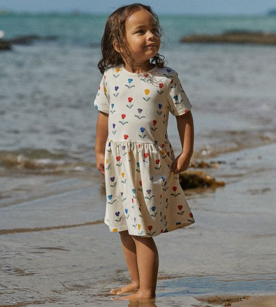 Young girl in a floral dress standing on a beach with ocean in the background