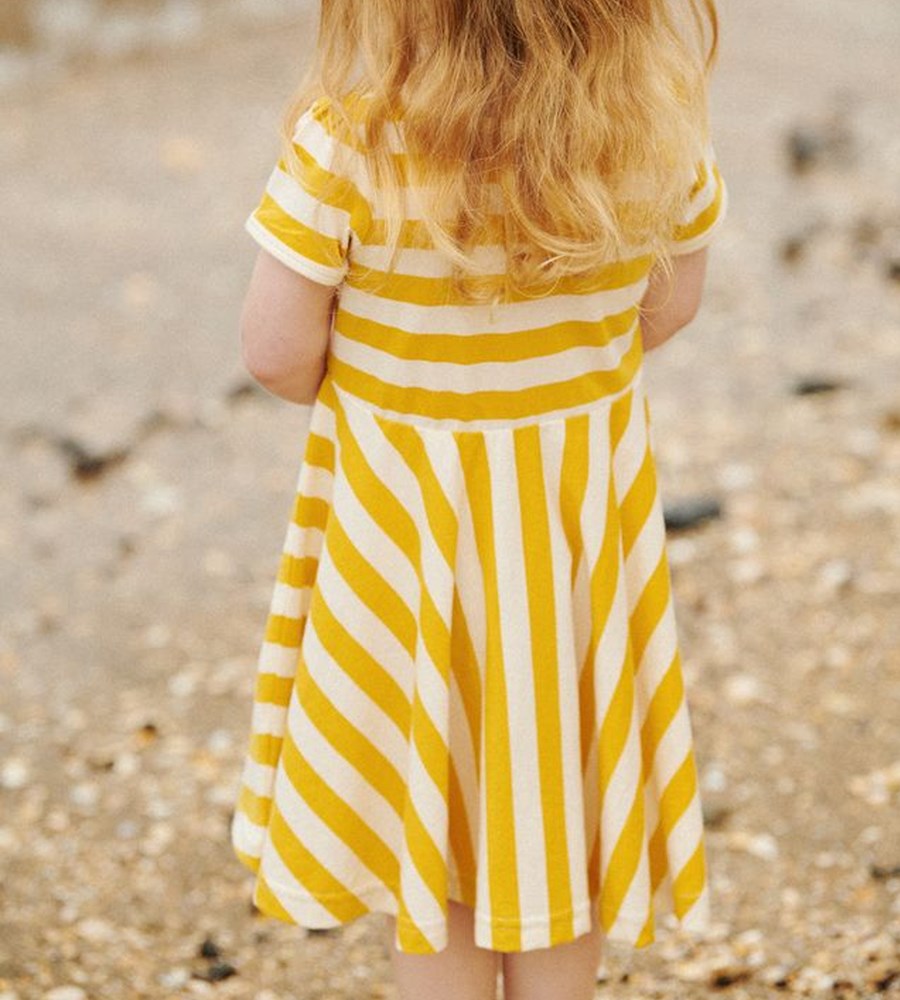 Child wearing a yellow and white striped dress on a beach.