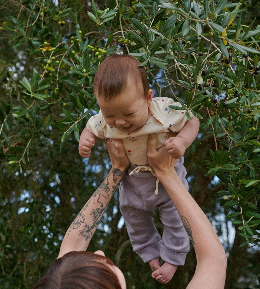 Person holding a baby against a backdrop of green foliage
