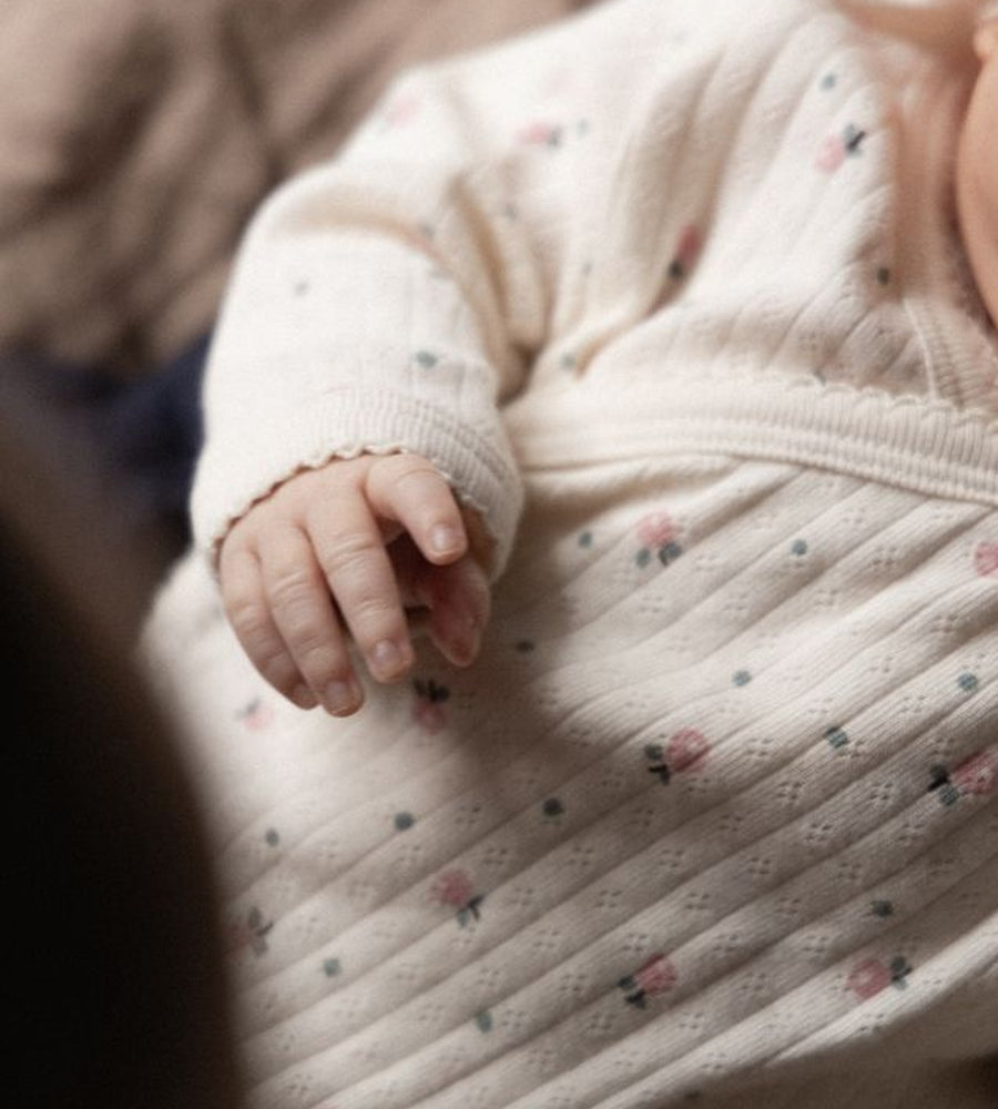 Close-up of a baby's hand and part of a pink textured garment with floral patterns.