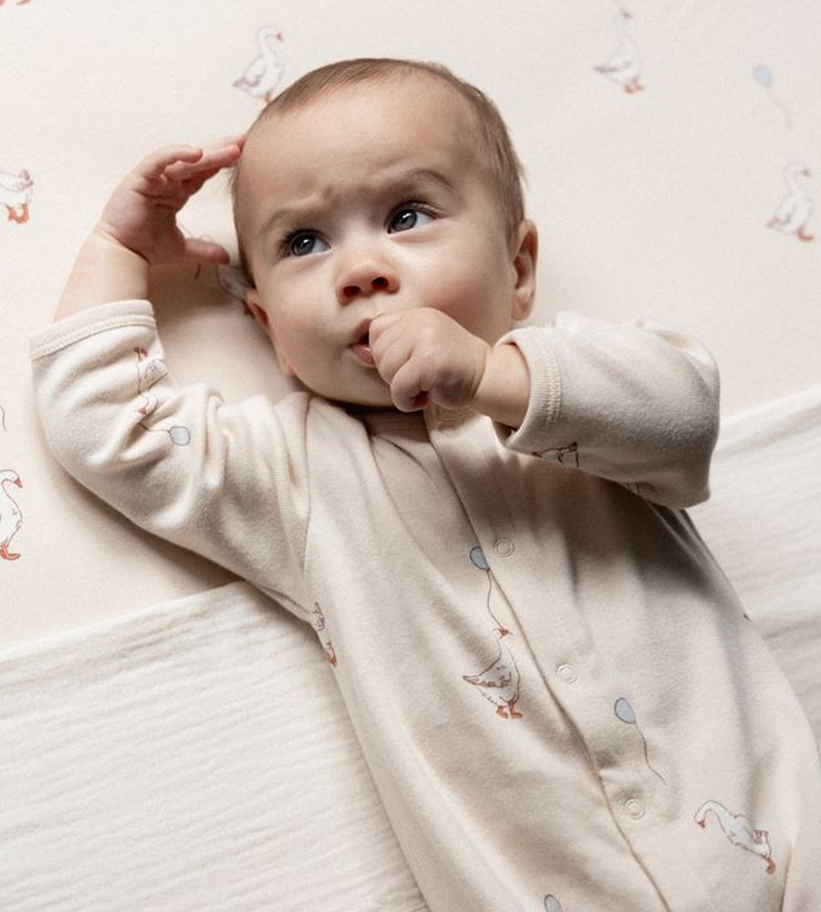 Baby wearing a light-colored onesie with small designs, lying on a soft surface.