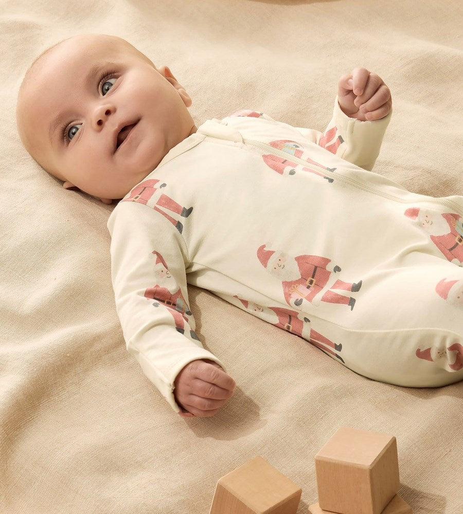 Baby lying on a beige blanket wearing a white onesie with pink fox patterns, surrounded by wooden blocks.