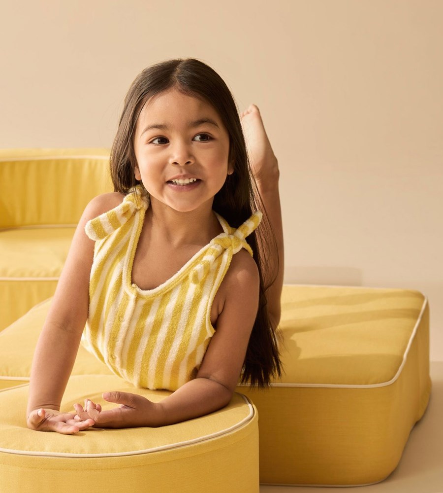 Young girl in a yellow outfit sitting on a yellow cushioned chair against a beige background