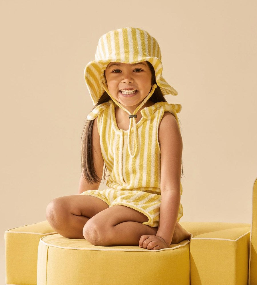 Child wearing a yellow striped outfit and hat sitting on a yellow chair against a beige background