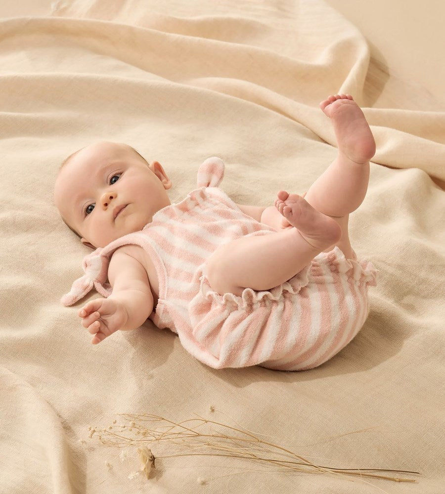 Baby in a pink striped outfit lying on a beige blanket
