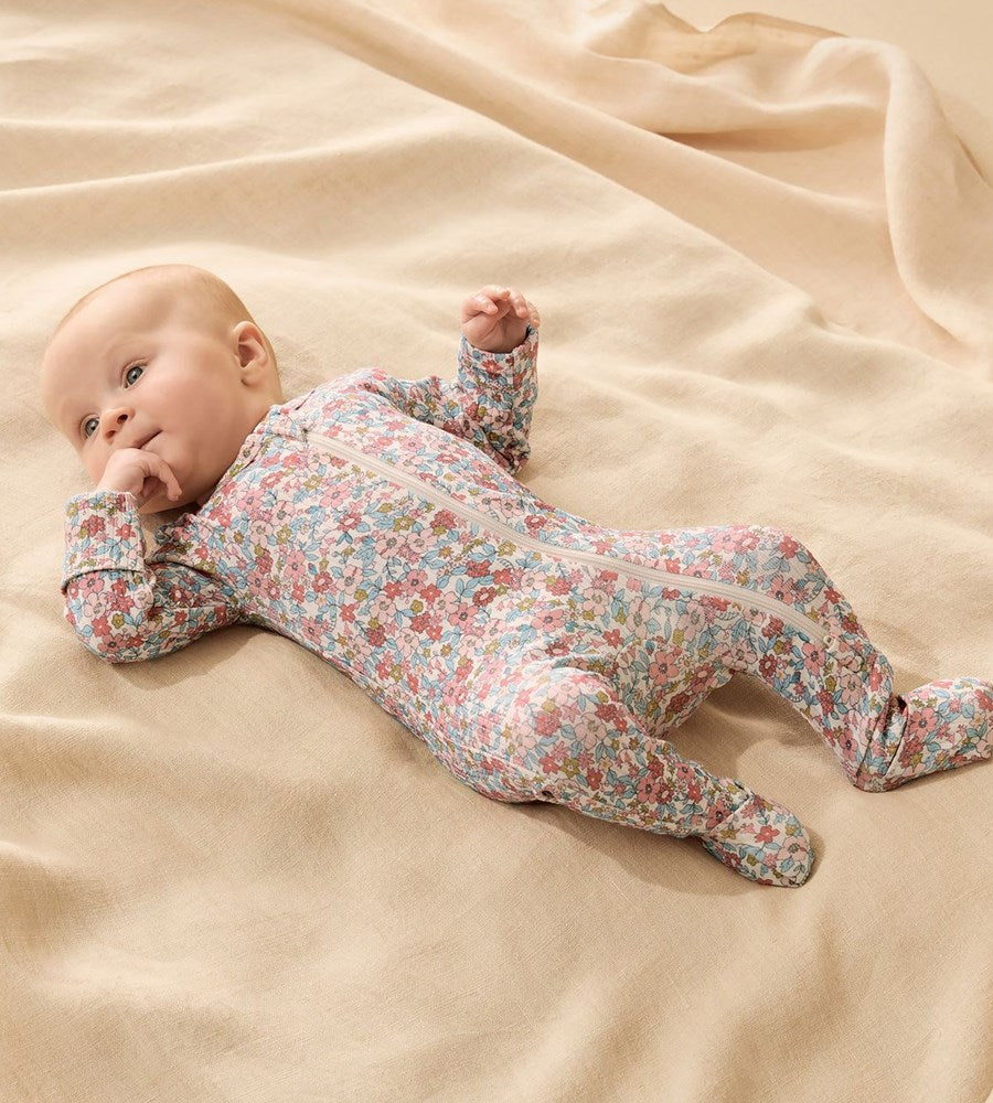 Baby lying on a beige blanket wearing a floral onesie.