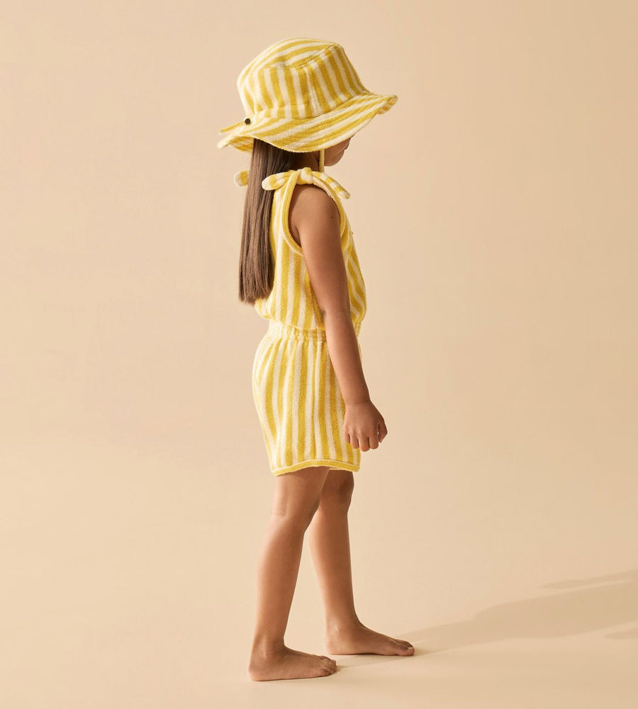 Child wearing a yellow striped dress and hat on a beige background