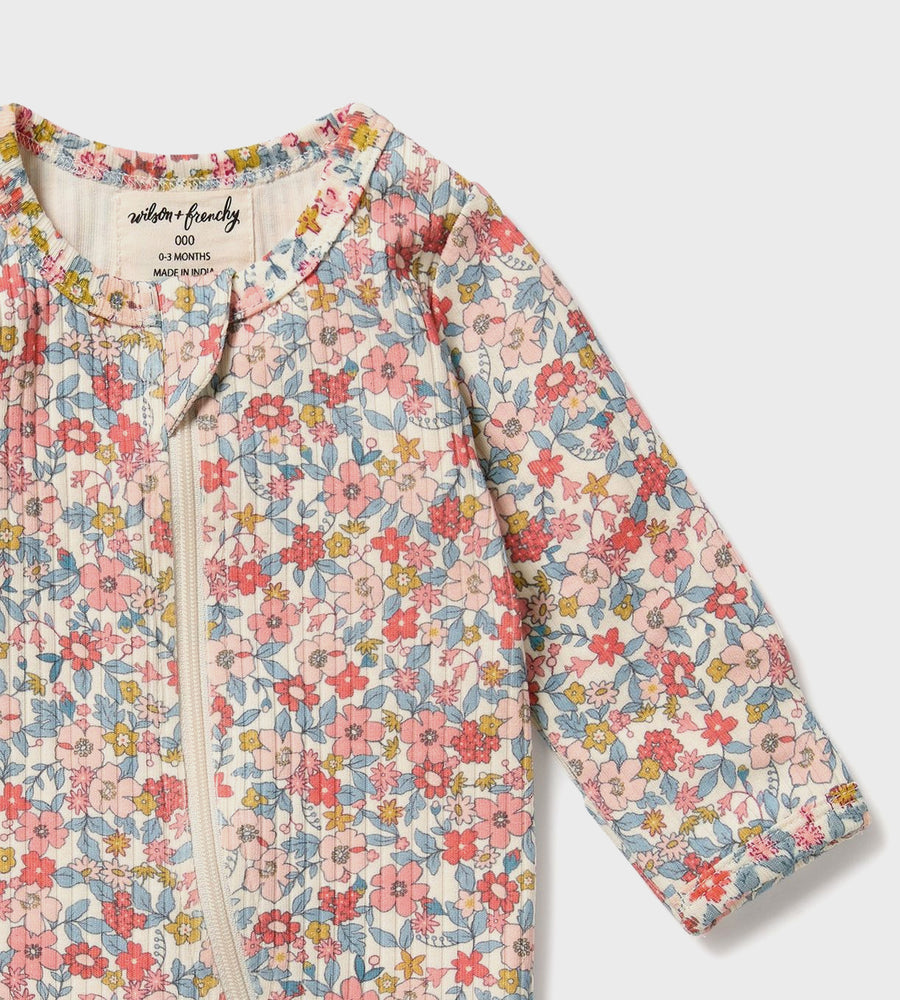 Floral patterned baby romper with brand label on a light gray background